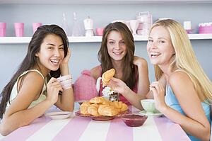 Three young woman sitting at a table having tea and a snack