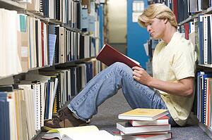 Man sitting on floor in library reading book