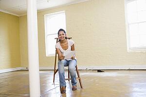 Woman sitting on ladder in empty space holding paper smiling