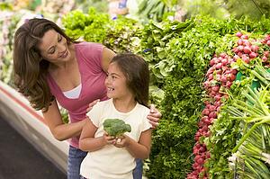 Mother and daughter shopping for broccoli at a grocery store