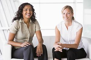 Two businesswomen sitting indoors smiling (high key/selective focus)
