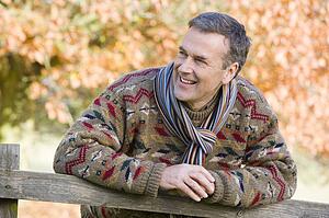 Man outdoors at park leaning on fence smiling (selective focus)