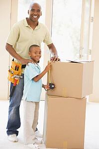 Father wearing tool belt standing by son and boxes in new home smiling