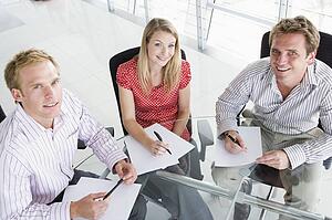 Three businesspeople in a boardroom with paperwork smiling