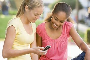 Teenage Girls Sitting Outside Playing With Mobile Phone