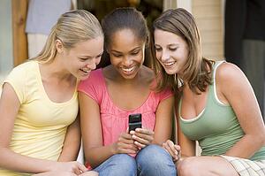 Teenage Girls Sitting Outside Playing With Mobile Phone