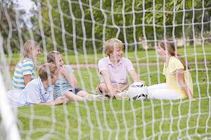 Five young friends on soccer field talking and smiling