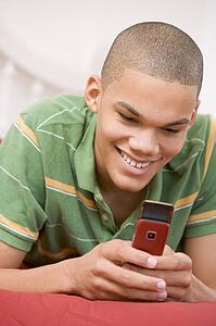 Teenage Boy Lying On Bed Using Mobile Phone 