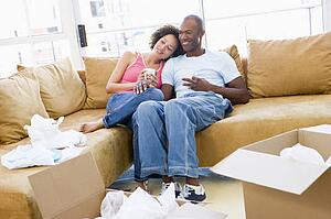Couple relaxing with coffee by boxes in new home smiling