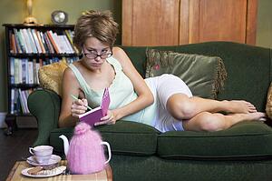 Young woman lying on sofa at home writing in her diary