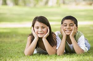 Two young children outdoors lying in park smiling (selective focus)