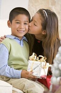 Sister Giving Her Brother A Christmas Present And Kissing Him On The Cheek