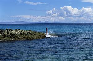 Woman outdoors standing on large rocks Oceanside (far away)