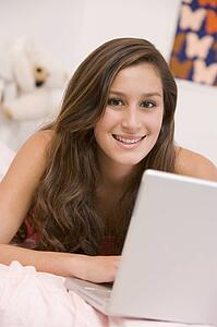 Teenage Girl Lying On Her Bed Using Laptop