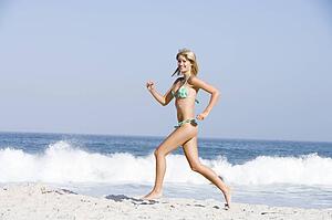 Woman in a two piece bathing suit running on a beach