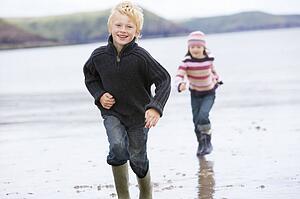 Two young children running on beach smiling
