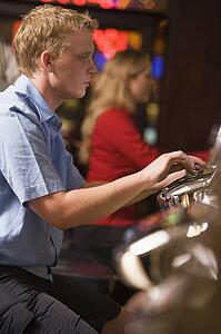 Man in casino playing slot machine with people in background (selective focus)