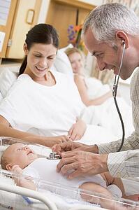 Doctor checking baby's heartbeat with new mother watching and smiling
