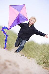 Young boy running on beach with kite smiling