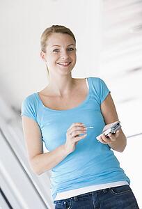 Woman standing in corridor using personal digital assistant smiling