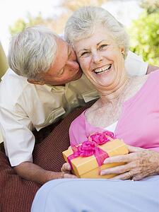Husband giving wife gift on patio kissing her and smiling