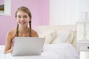 Teenage Girl Lying On Bed Using Laptop 