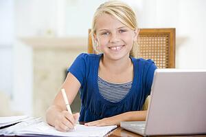Young girl with laptop doing homework in dining room smiling