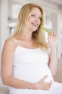 Pregnant woman eating celery and smiling