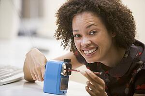 Woman in computer room using pencil sharpener and smiling