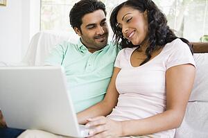 Couple in living room with laptop smiling (high key/selective focus)