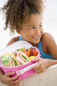 Young girl holding packed lunch in living room smiling