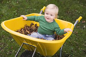 Baby outdoors sitting in wheelbarrow smiling (selective focus)