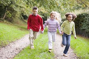 Three young friends running on a path outdoors smiling