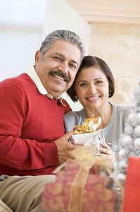 Middle Aged Couple Sitting On Sofa Holding Christmas Present