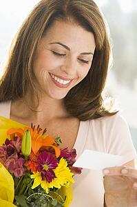 Woman holding flowers and reading note smiling