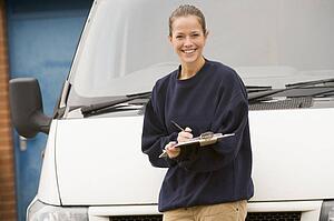 Deliveryperson standing with van writing in clipboard smiling