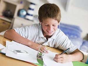 Young Boy Doing His Homework While Listening To Music On His MP3 Player