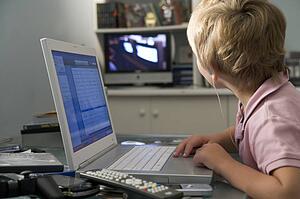 Young boy in bedroom using laptop and listening to MP3 player