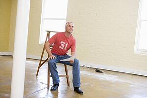 Man sitting on ladder in empty space holding paper