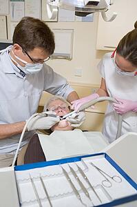 Dentist and assistant in exam room with woman in chair