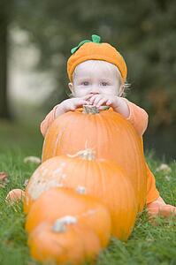 Baby boy outdoors in pumpkin costume with real pumpkins
