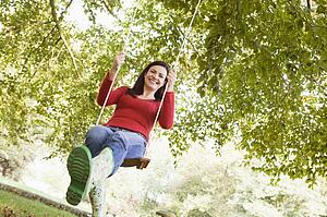 Woman outdoors on tree swing smiling (high key/selective focus)