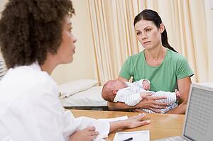 Doctor with laptop and woman in doctor's office holding baby