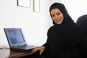 Woman in office with laptop smiling (high key/selective focus)