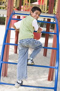 Young boy climbing on playground structure smiling (selective focus)