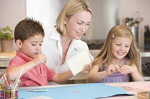 Woman and two young children in kitchen with art project smiling