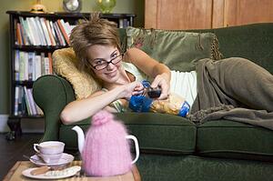 Young woman lying on sofa at home eating potato chips and watching television