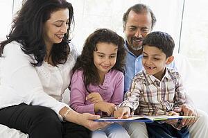 Grandparents sitting in living room reading with grandchildren smiling (high key)