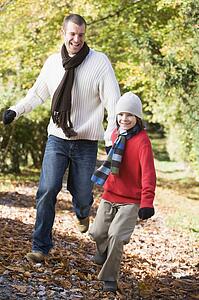 Man and young boy running outdoors in park and smiling