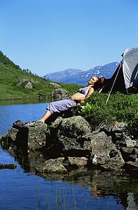 Woman outdoors at campsite sleeping on large rocks by lake